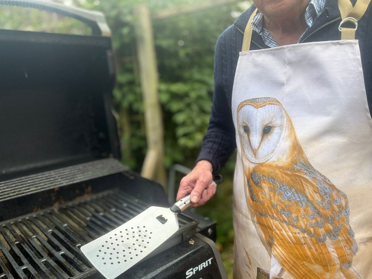 man holding spatula wearing barn owl apron with BBQ