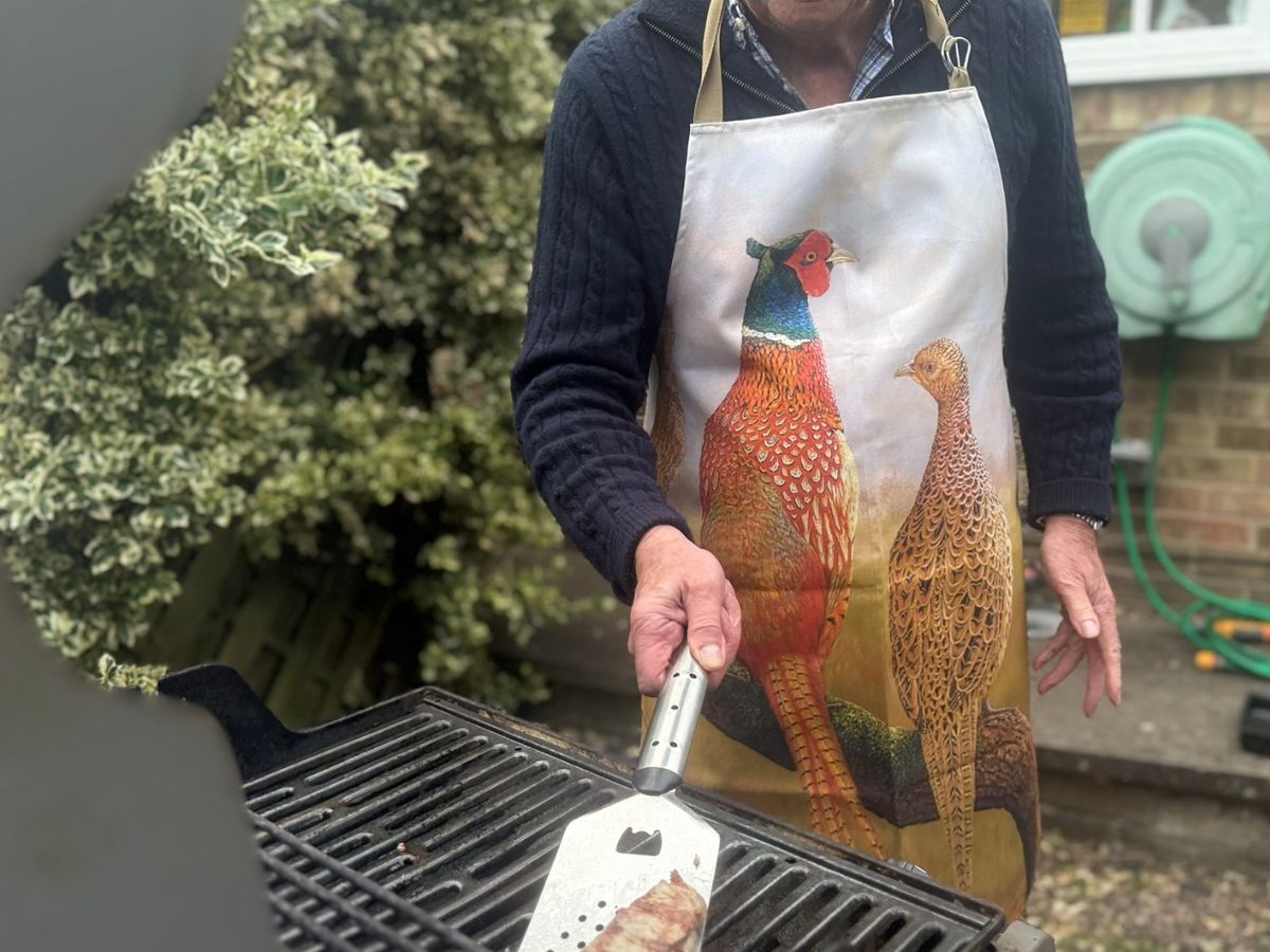 man wearing apron featuring courting pheasant painting by Robert E Fuller holding BBQ spatula