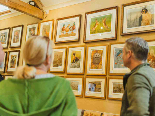 Two people looking at framed pictures on a wall in an art gallery.