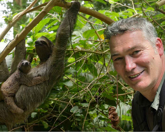 Artist Robert E Fuller smiling next to a sloth in the Panama rainforest