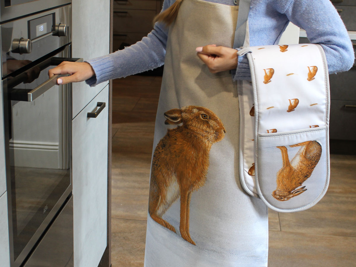 person wearing apron with oven glove over arm opening oven door