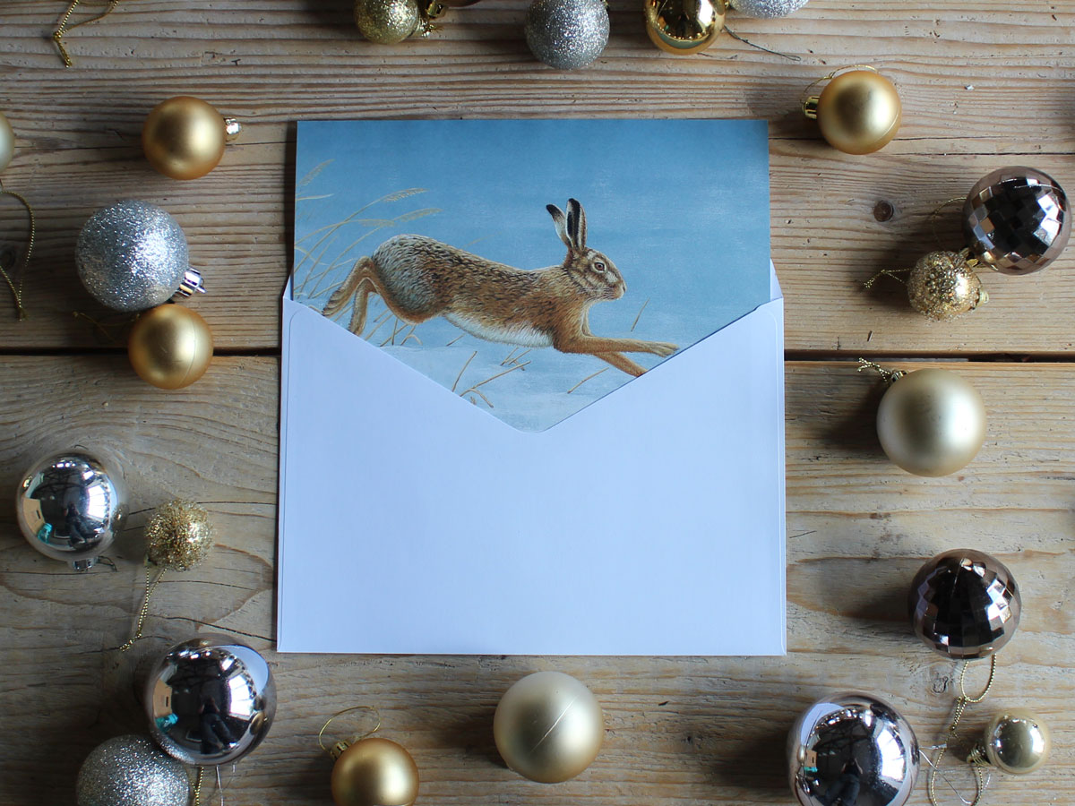 christmas card of hare in snow surrounded by silver baubles