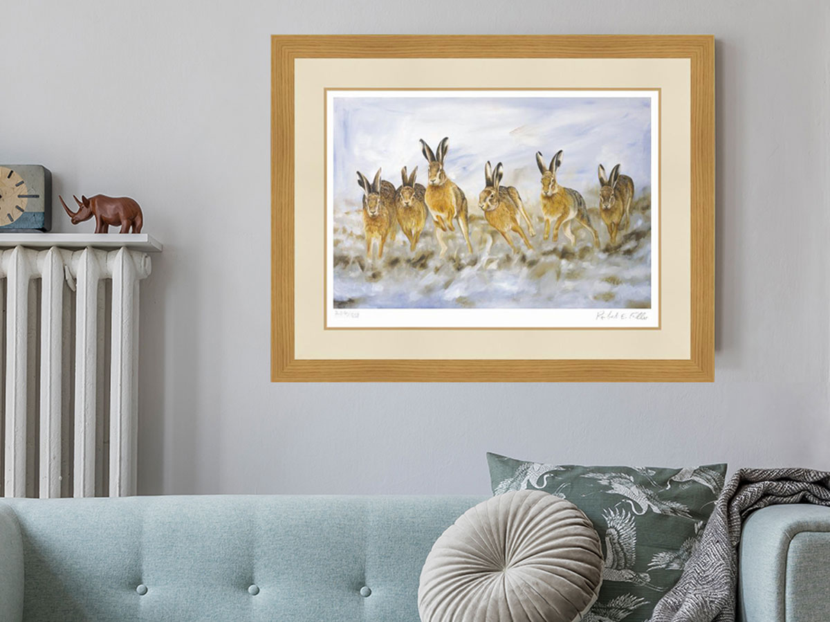 framed painting of hares running through snow on wall above green sofa with cushions