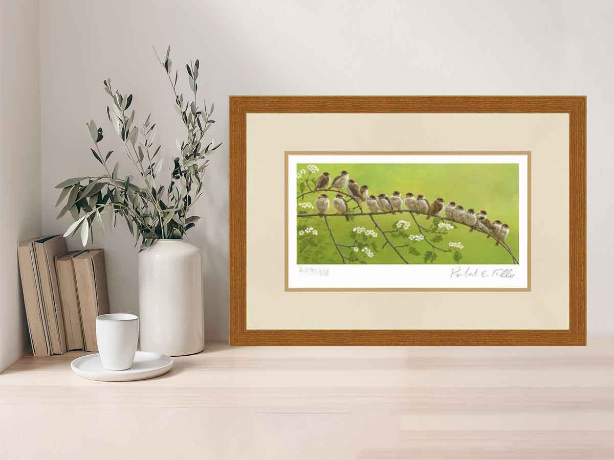 Framed art print featuring line of tree sparrows perched on hawthorn branch on shelf with coffee cup, books and vase of dried leaves