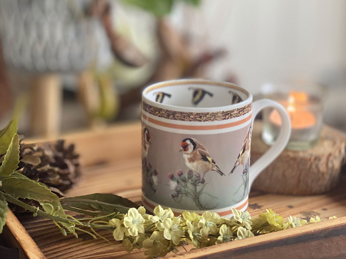 mug with goldfinch on tray with flowers and candle behind
