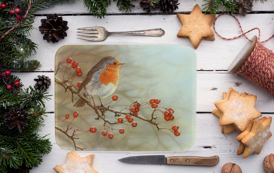 glass work top saver featuring robin on a branch surrounding the chopping board is a knife, biscutis, roll of string, fork and ever green leaves, hawthorn berries and cones