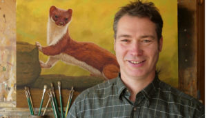 Wildlife artist, Robert E Fuller standing at the easel with an oil painting behind him that he has produced of a stoat called Crackle