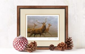 painting of stag and two hinds framed in dark wood with christmas baubles and pine cones in foreground